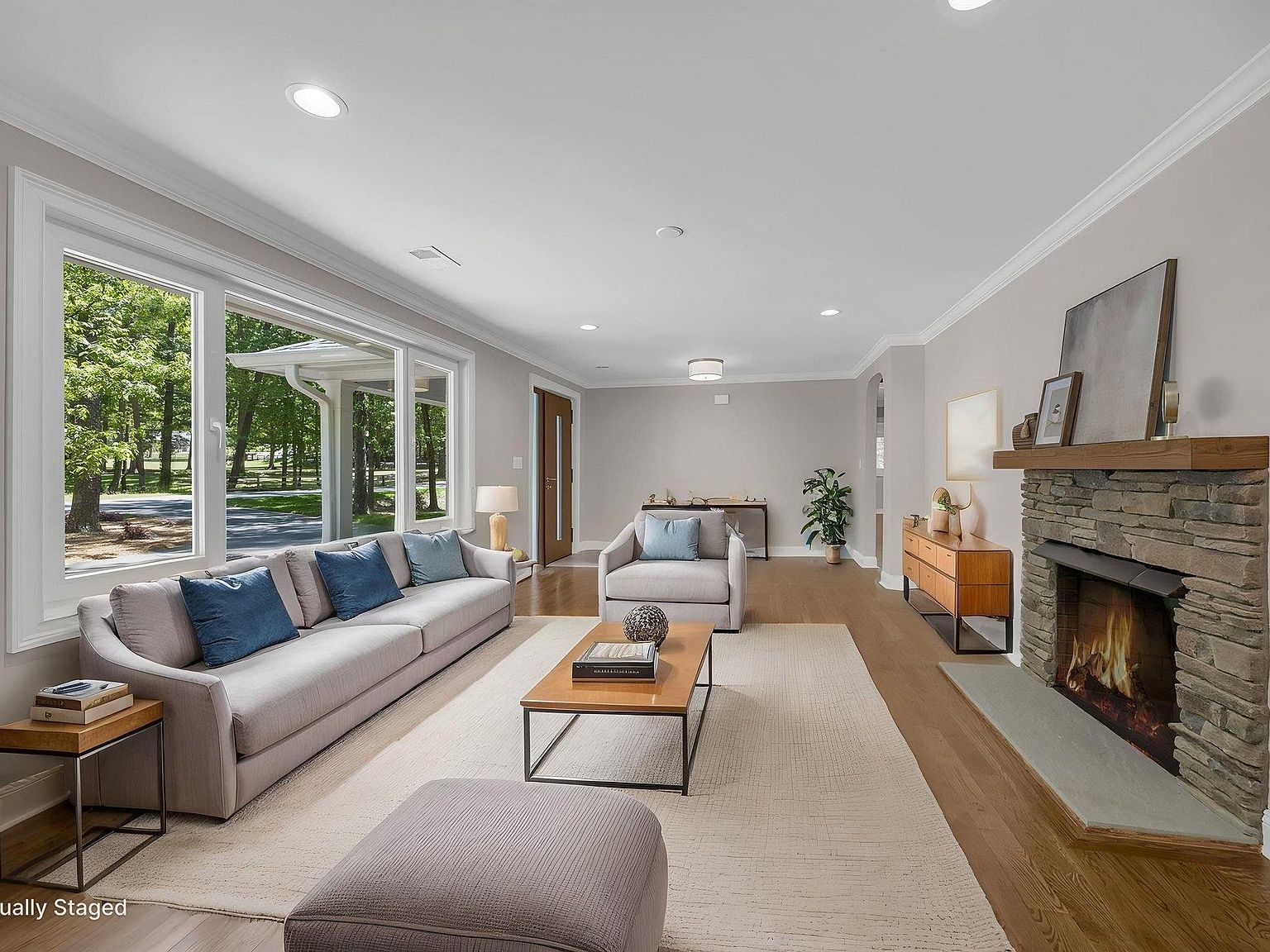 Great room with stone fireplace, gray sectional, and tall windows overlooking the front lawn