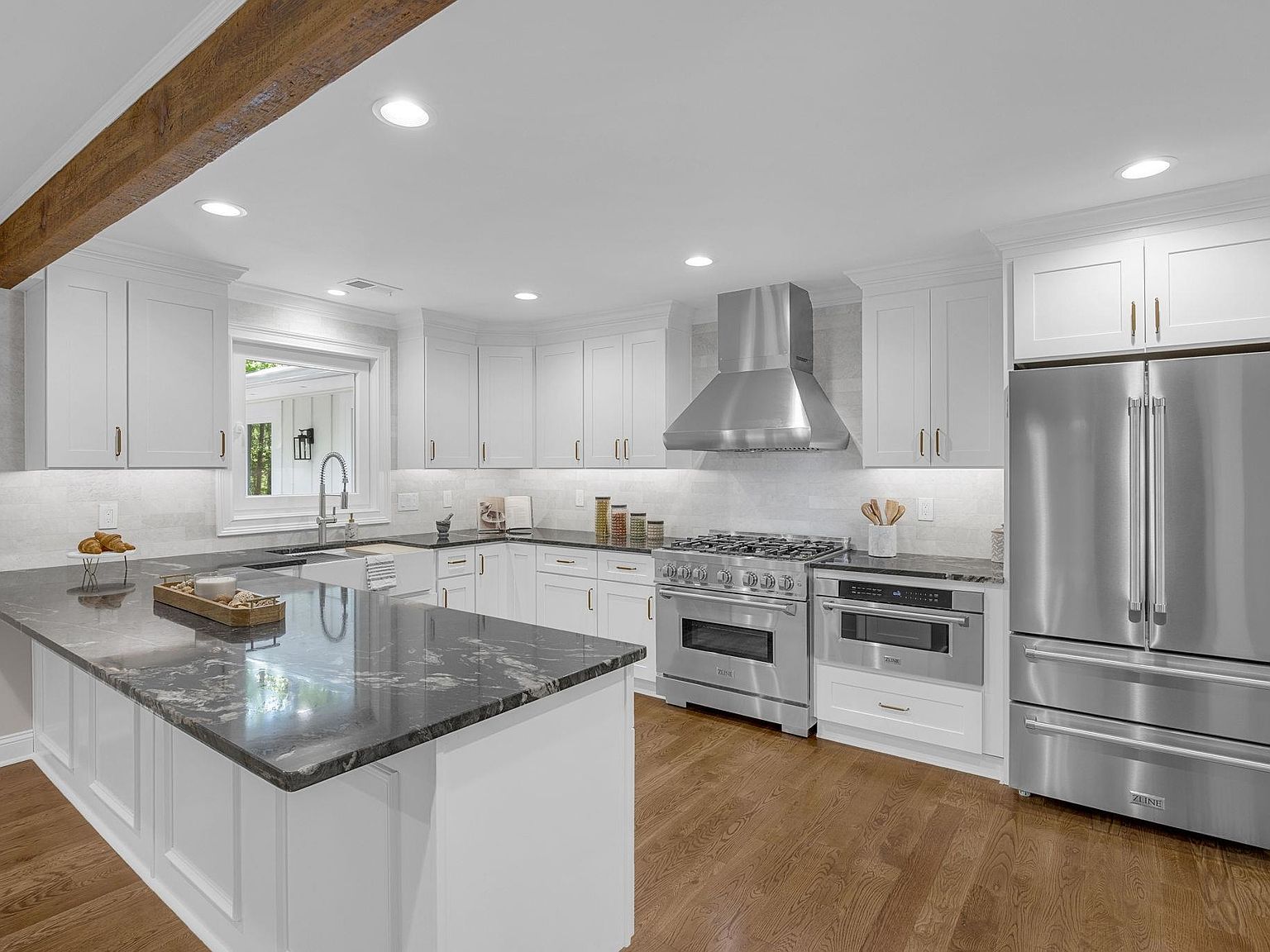 Wide view of the white-cabinet ZLINE kitchen with stainless gas range, hood, and stone-topped island