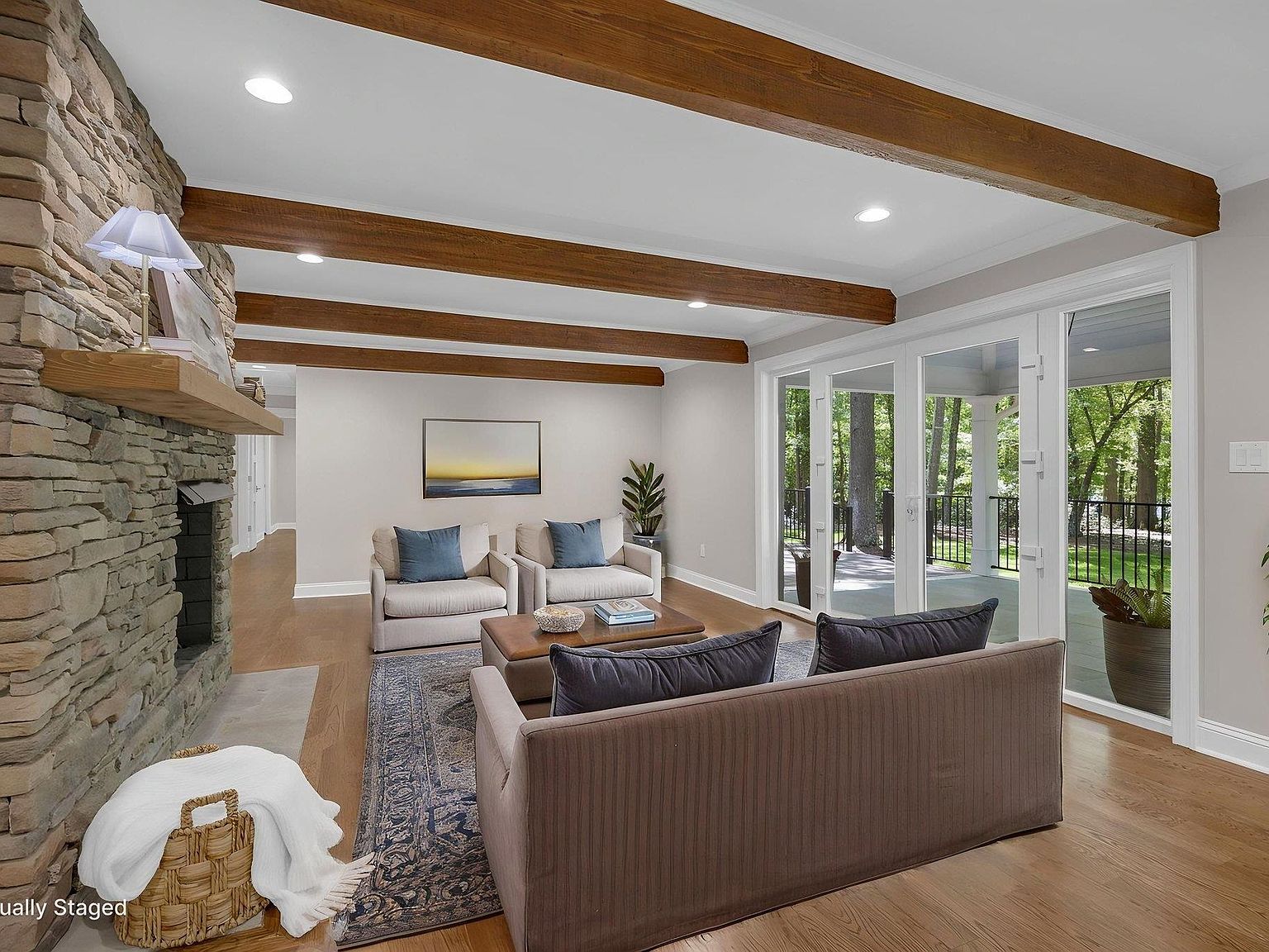 Family room with full ceiling of wood beams, stacked-stone fireplace, and French doors to the back porch