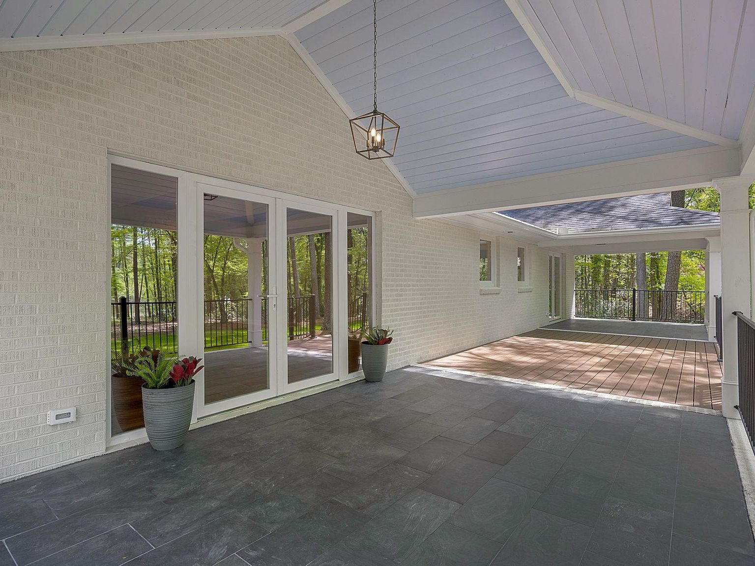 Covered back porch with vaulted shiplap ceiling, slate tile floor, and forest views on three sides