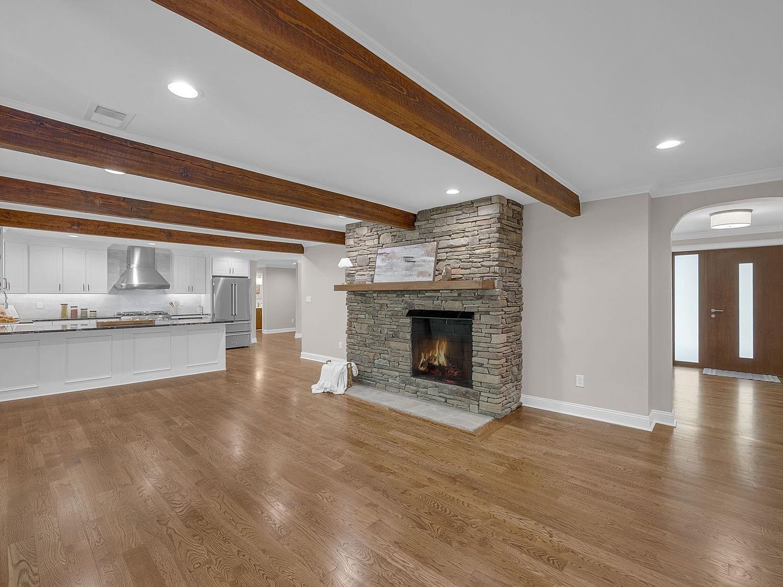 Open-concept living wing with stacked-stone fireplace anchoring beamed ceiling and oak floors